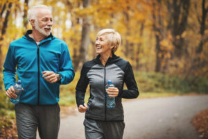 Closeup front view of a senior couple jogging in a forest and having fun. 